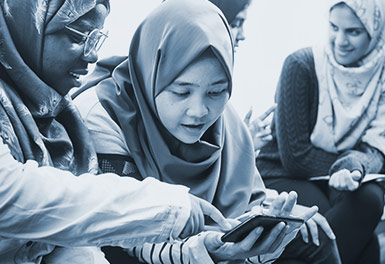 Young women sit talking looking at something on a smart phone