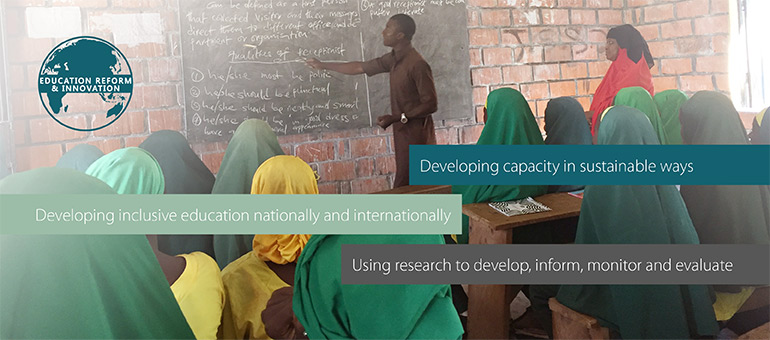 In a school in Africa a classroom of girls are looking towards a teacher writing on a chalkboard.