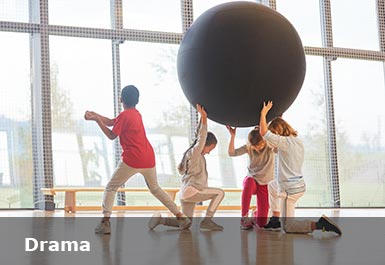 In a drama hall three children hold a giant globe above their heads another child is dancing