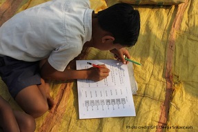 Boy sits doing homework on carpet India