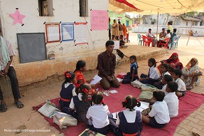 Male teachers gives a class to students outside on a carpet India