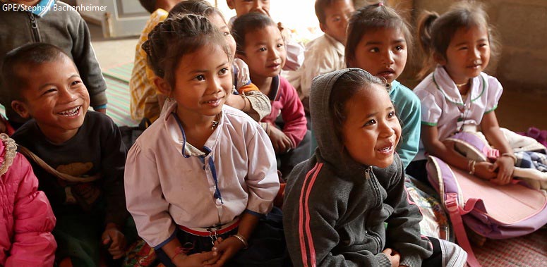 children sit on a classroom floor looking up and smiling happily