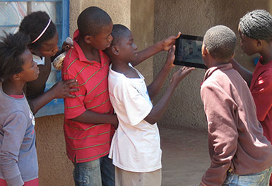 a group of girls and boys standing and looking at a digital tablet