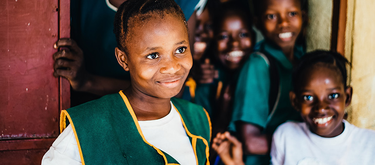 A school girl and some friends stand in a doorway smiling