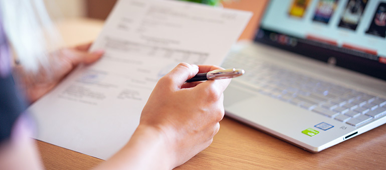 a person works at a desk with pen paper and a laptop 